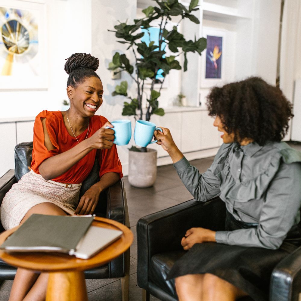 Two friends sharing a cup of tea together, smiling.