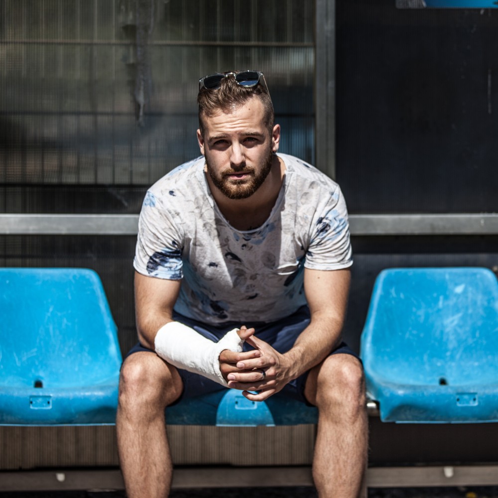 Injured man with arm cast sitting on blue stadium seats