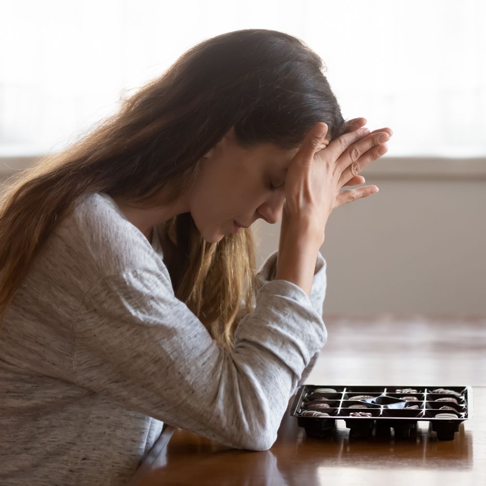 Distressed woman holds head near box of chocolates