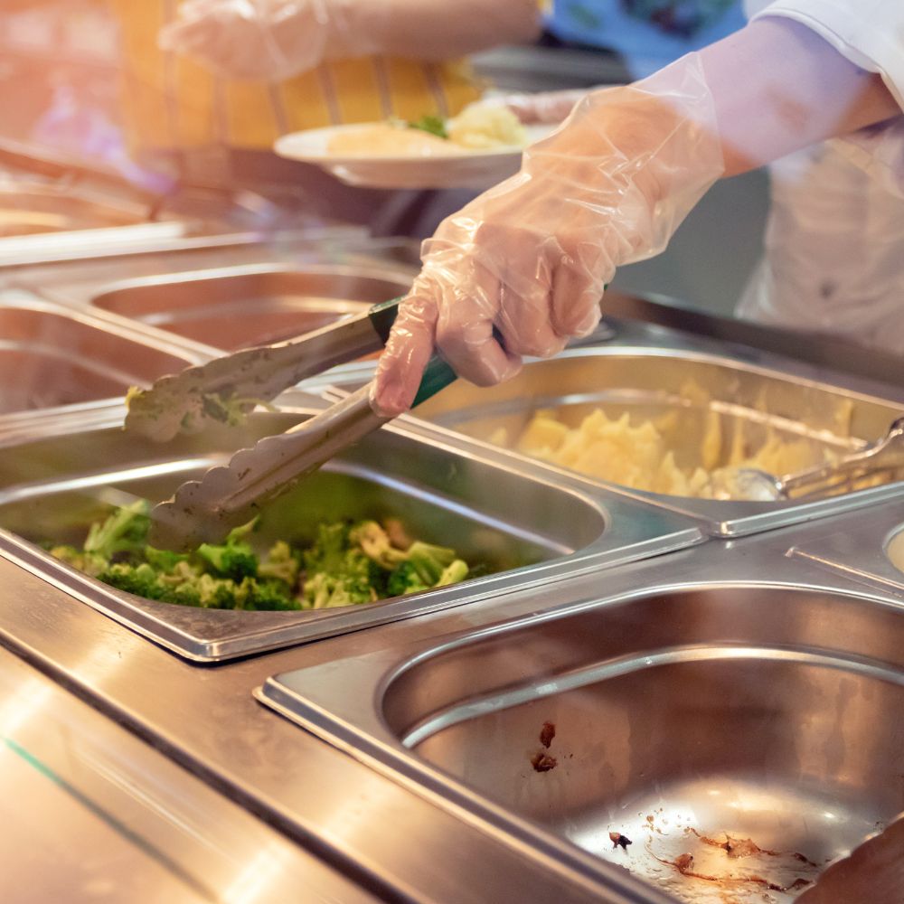 Cafeteria worker serving vegetables onto student’s plate