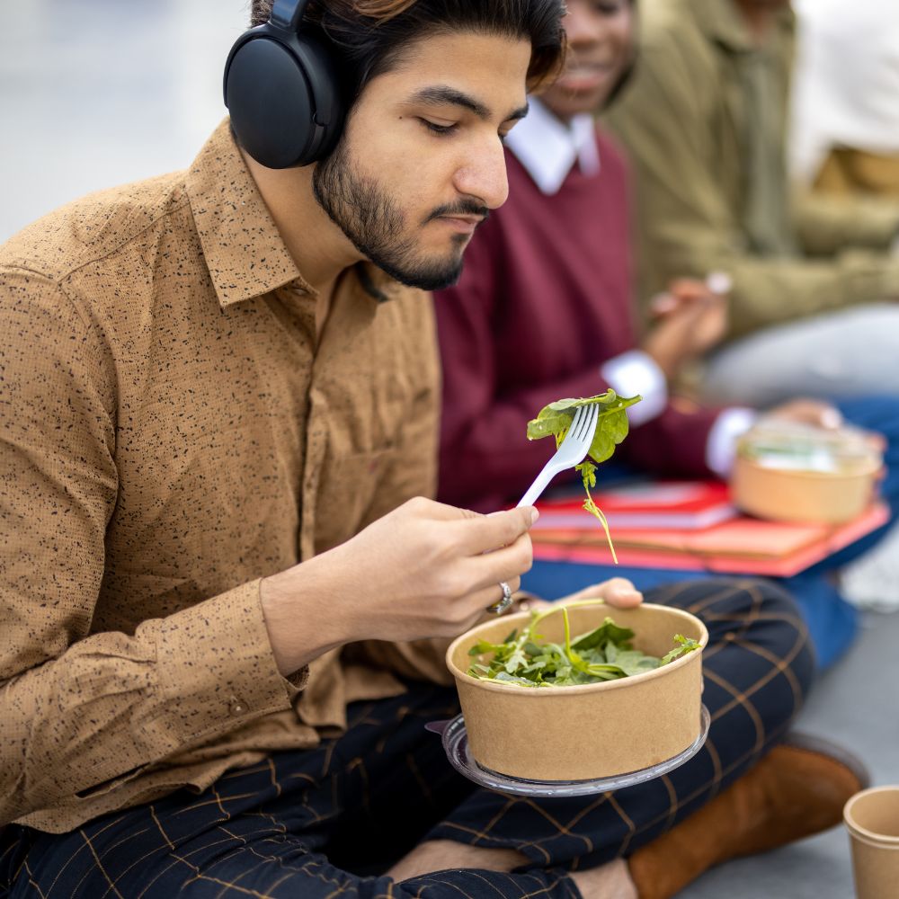 Student eating salad while sitting outside with peers