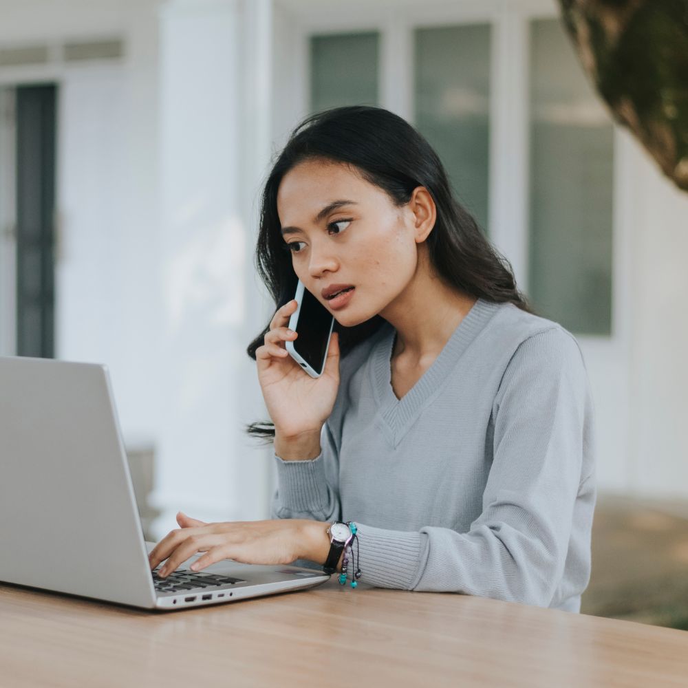 Student on phone while working on laptop outdoors
