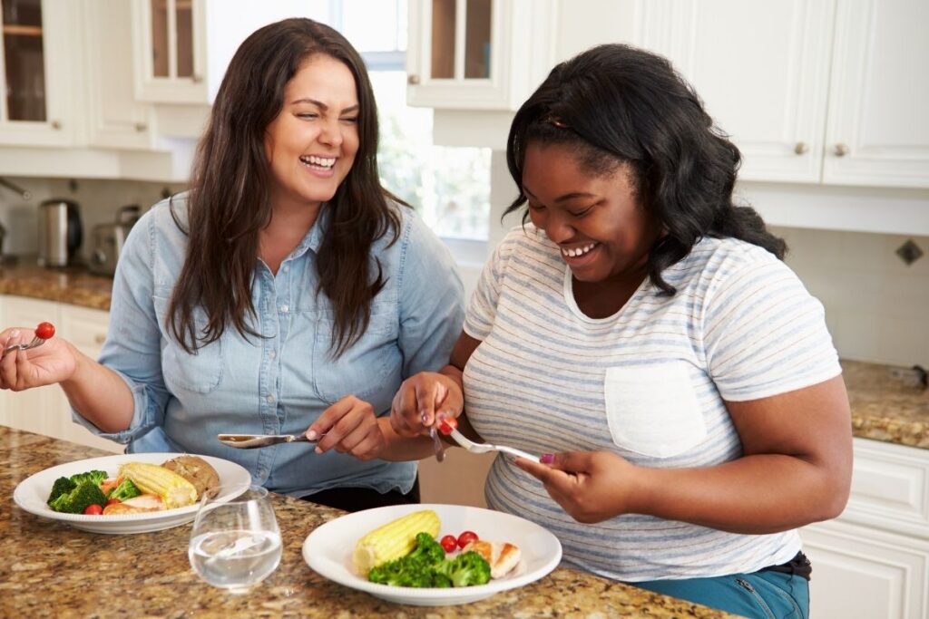 Two women enjoying a healthy meal together in a kitchen while laughing and smiling