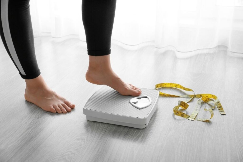 Person cautiously stepping onto a scale with a yellow measuring tape nearby