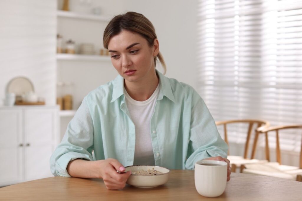 Woman with a blank expression staring at a bowl of oatmeal