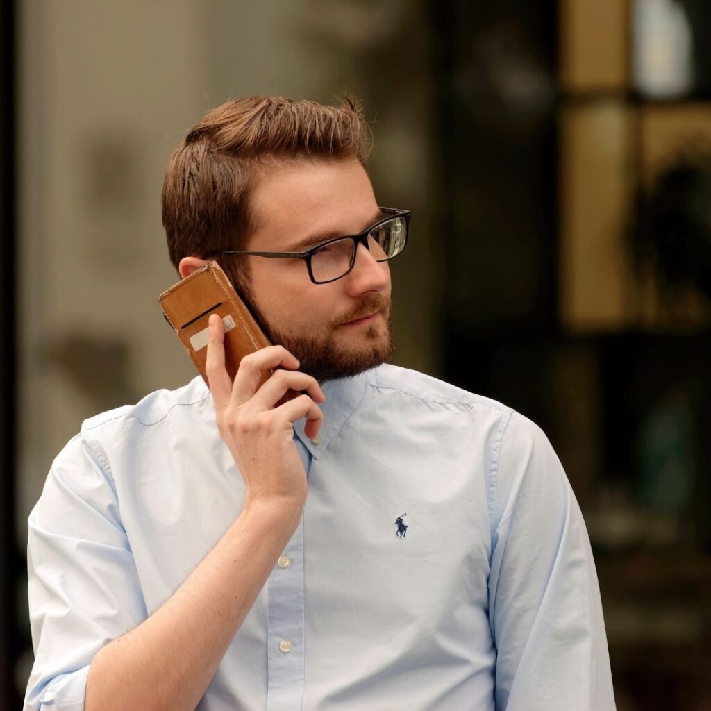 A man in a light blue shirt holds a phone to his ear while standing outdoors
