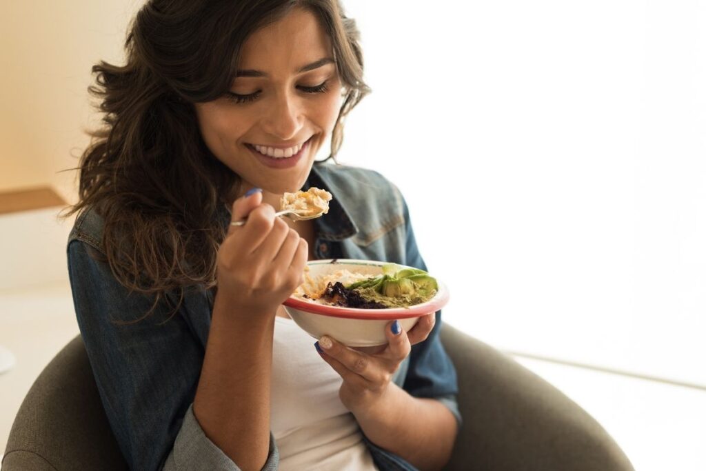 Woman smiling while eating a nourishing bowl of food with avocado and grains