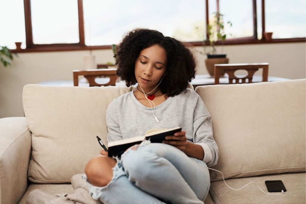 Woman sitting on a couch listening to music and journaling