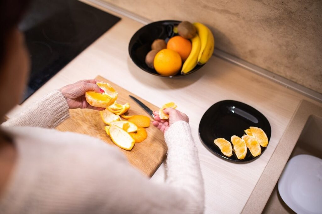 Person peeling and segmenting an orange on a cutting board, preparing a plate of fresh fruit