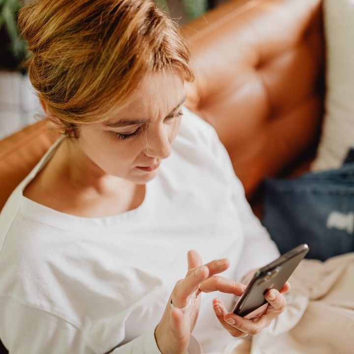 Woman sitting on couch, looking at smartphone screen with focused expression and furrowed brow