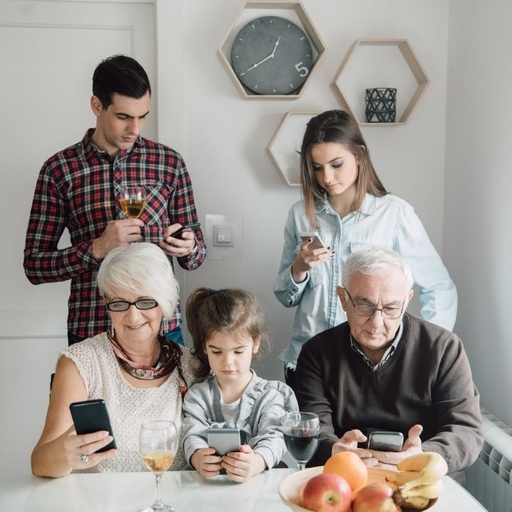 Family of all ages sitting and standing, each person focused on their own smartphone screen
